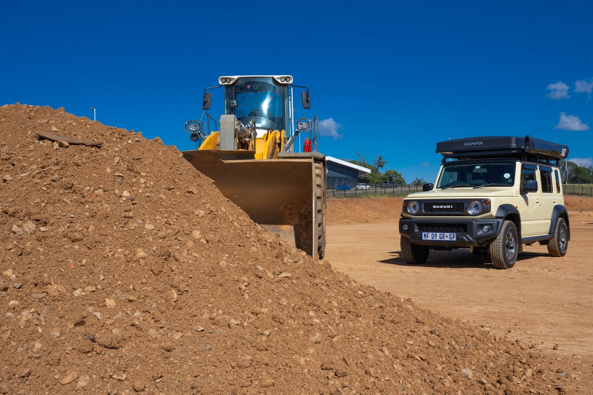 Cream Suzuki Jimny with tractor in front of a heap of soil